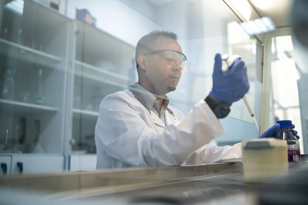 Técnico de laboratório de óculos e luvas pipetando uma amostra